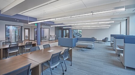 Open office layout with modern furniture, including workstations, collaborative seating areas, and bright overhead lighting.
