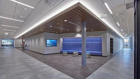 Modern office lobby with soft lighting, purple accent walls, and a seating area with minimalist chairs and a large screen display.