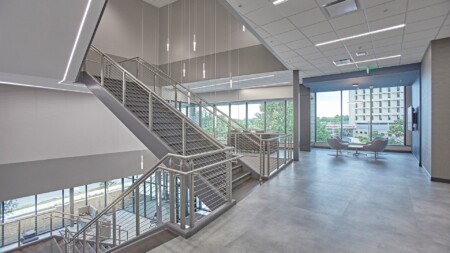 Modern office space with an industrial staircase, large windows, and bright lighting.