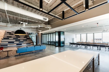 Modern office interior featuring a stylish blue couch, a staircase with integrated lighting, and glass meeting rooms that showcase a professional workspace.