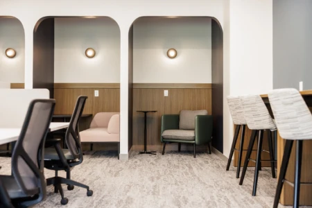 Modern office interior featuring stylish seating areas with archways, ergonomic chairs, and wooden accents. The design includes a cozy green chair and a pink sofa, complemented by soft lighting and a sleek table, creating a productive and inviting workspace.