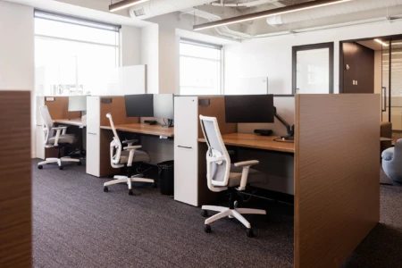Modern office workspace featuring ergonomic chairs and dual-monitor setups in an open layout with plenty of natural light.