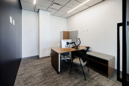 Modern office workspace featuring a desk with a computer, ergonomic chair, and a cozy seating area, designed for productivity and comfort. The room is well-lit with neutral colors and contemporary furnishings, ideal for focused work or meetings.
