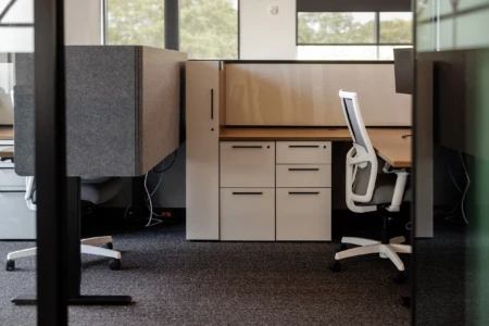 Modern office workspace featuring ergonomic chairs, gray cubicle partitions, and a sleek desk with storage drawers, designed for productivity and comfort.