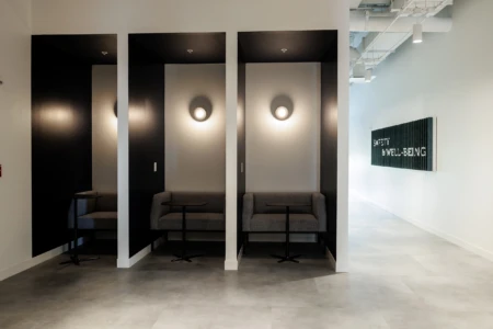 Modern interior of a wellness space featuring cozy gray seating areas with side tables and a wall art sign about safety and well-being.