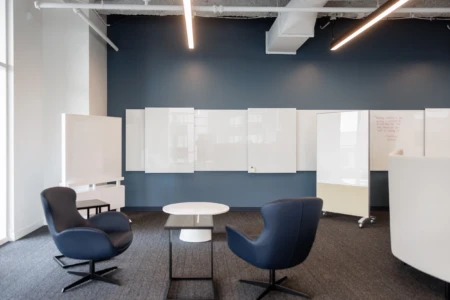 Modern office meeting space featuring a minimalist design with navy walls, comfortable chairs, and whiteboards for collaboration.