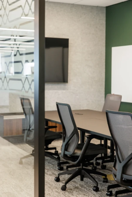 Modern conference room featuring a large table and ergonomic office chairs, equipped with a wall-mounted TV and whiteboard, designed for collaborative meetings.