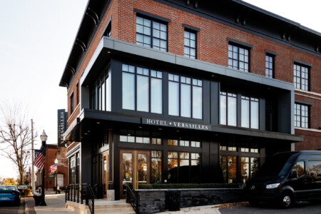 Exterior view of Hotel Versailles, showcasing its modern architectural design, large windows, and welcoming entrance on a charming street.