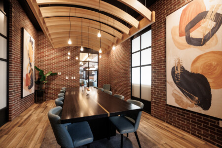 Modern conference room featuring a long wooden table, stylish blue chairs, exposed brick walls, and artistic wall decor under a curved wooden ceiling with pendant lights.