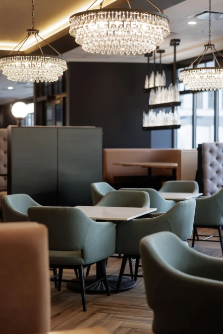 Elegant dining area featuring plush green chairs, marble tables, and sparkling chandeliers. The decor is modern with a sophisticated atmosphere.