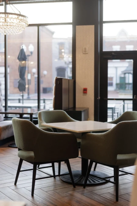 Chic cafe interior with modern chairs and table, large windows offering a view of street, ambient lighting from elegant chandelier.