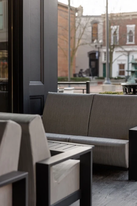 A cozy cafe setting with modern furniture, overlooking a street view of historic brick buildings and lampposts through large windows.