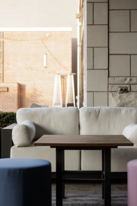 Outdoor seating area featuring a white sofa, wooden table, and colorful cushions, set against a brick wall backdrop. Peaceful and inviting atmosphere.