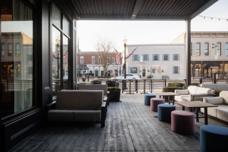 A cozy outdoor seating area with modern furniture overlooks a quiet street lined with historical buildings and shops. Flags add a vibrant touch.