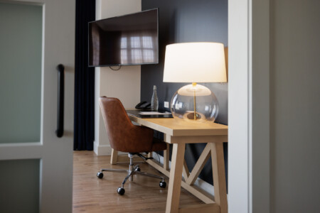 Modern workspace featuring a wooden desk with a stylish brown chair, a clear glass lamp, and a flat-screen TV mounted on the wall, creating a cozy and functional environment.