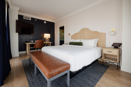 Modern hotel room featuring a comfortable bed, wooden headboard, and stylish furnishings including a desk, a leather bench, and a mounted TV.