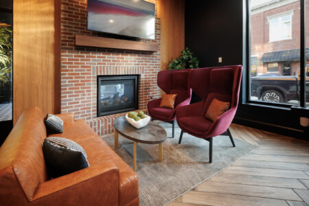 Cozy modern lounge area featuring a brick fireplace, stylish maroon chairs, a leather sofa, and a contemporary coffee table, ideal for relaxation.
