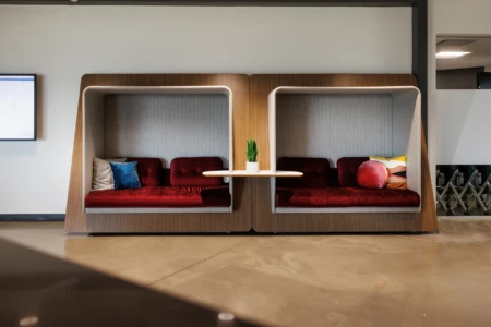 Modern office seating area featuring two stylish, enclosed booths with plush red cushions and a small table, ideal for collaborative work or casual meetings.