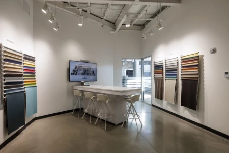 Modern interior design studio with sample fabrics on the walls, a central white island, and chairs under bright track lighting.