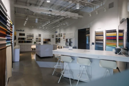Modern interior of a medical and dental fabric showroom featuring a variety of colorful fabric samples displayed on walls and countertops, with sleek white furniture and ample lighting.