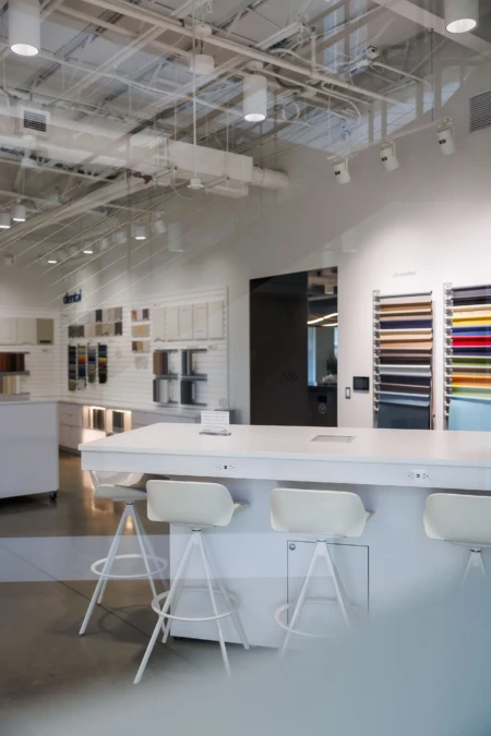 Modern interior design showroom featuring a sleek white consultation table with stylish stools and a wall displaying various material samples.