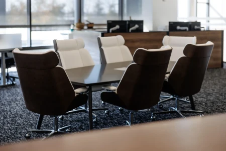Modern conference room featuring a sleek black table surrounded by ergonomic chairs with a combination of dark wood and white upholstery, designed for professional meetings. Large windows provide natural light, enhancing the workspace ambiance.