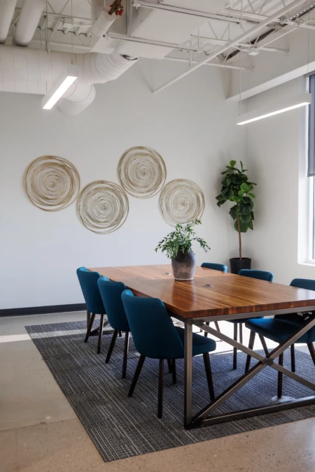 Conference room with a wooden table, blue upholstered chairs, modern wall decor, and a potted plant centerpiece.