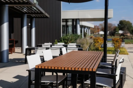 Outdoor dining area with wooden table and white chairs.